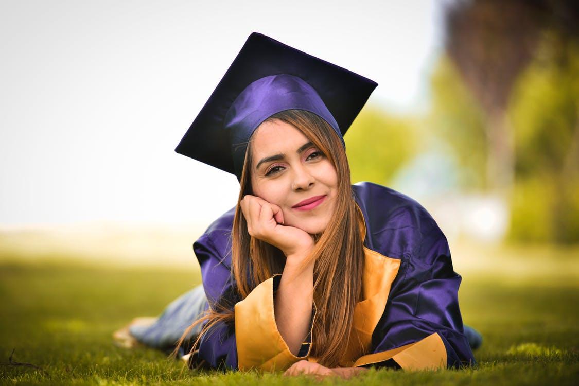 Woman Wearing Purple Graduation Gown Lying on Field
